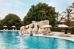 A swimming pool with lounge chairs and umbrellas, surrounded by rocks and trees.
