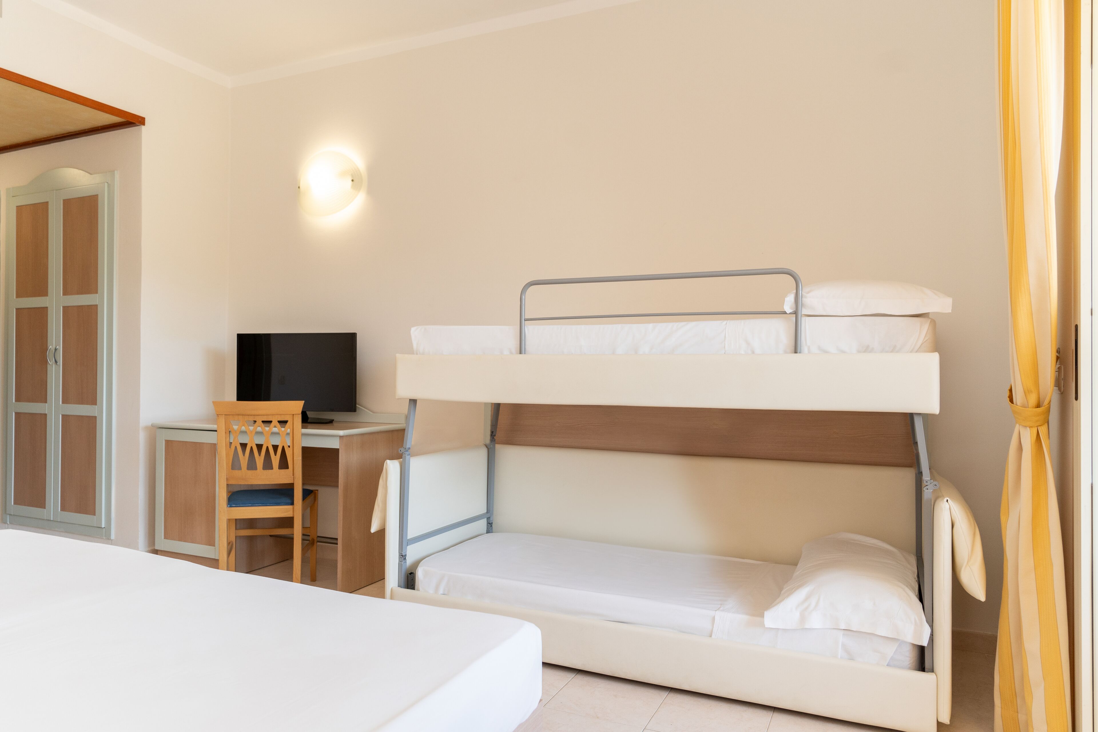 A bunk bed with a desk and chair, a television, and a door with a window.