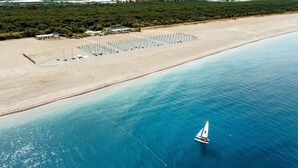 Vista aérea de una playa con un velero, una fila de sombrillas y un edificio con techo.