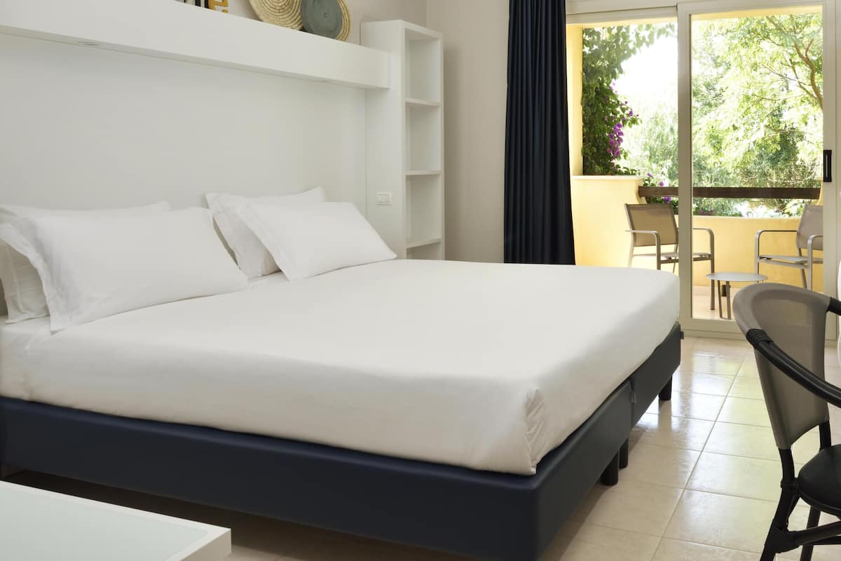 A hotel room with a large bed, a desk, and a balcony with outdoor seating.