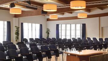 Ein Konferenzraum mit Reihen von Stühlen, einem großen Tisch und hängenden, orangefarbenen Leuchten.