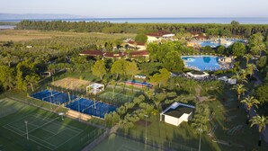 Vista aérea de un resort con una gran piscina, canchas de tenis y una vista panorámica al océano.