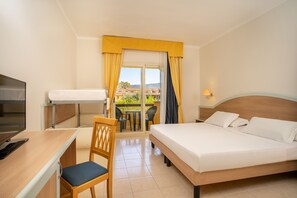 A hotel room with a bed, desk, chair, TV, and a balcony with a view of houses.
