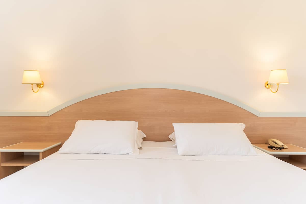 A neatly made bed with white linens, two bedside tables, and a wooden headboard.