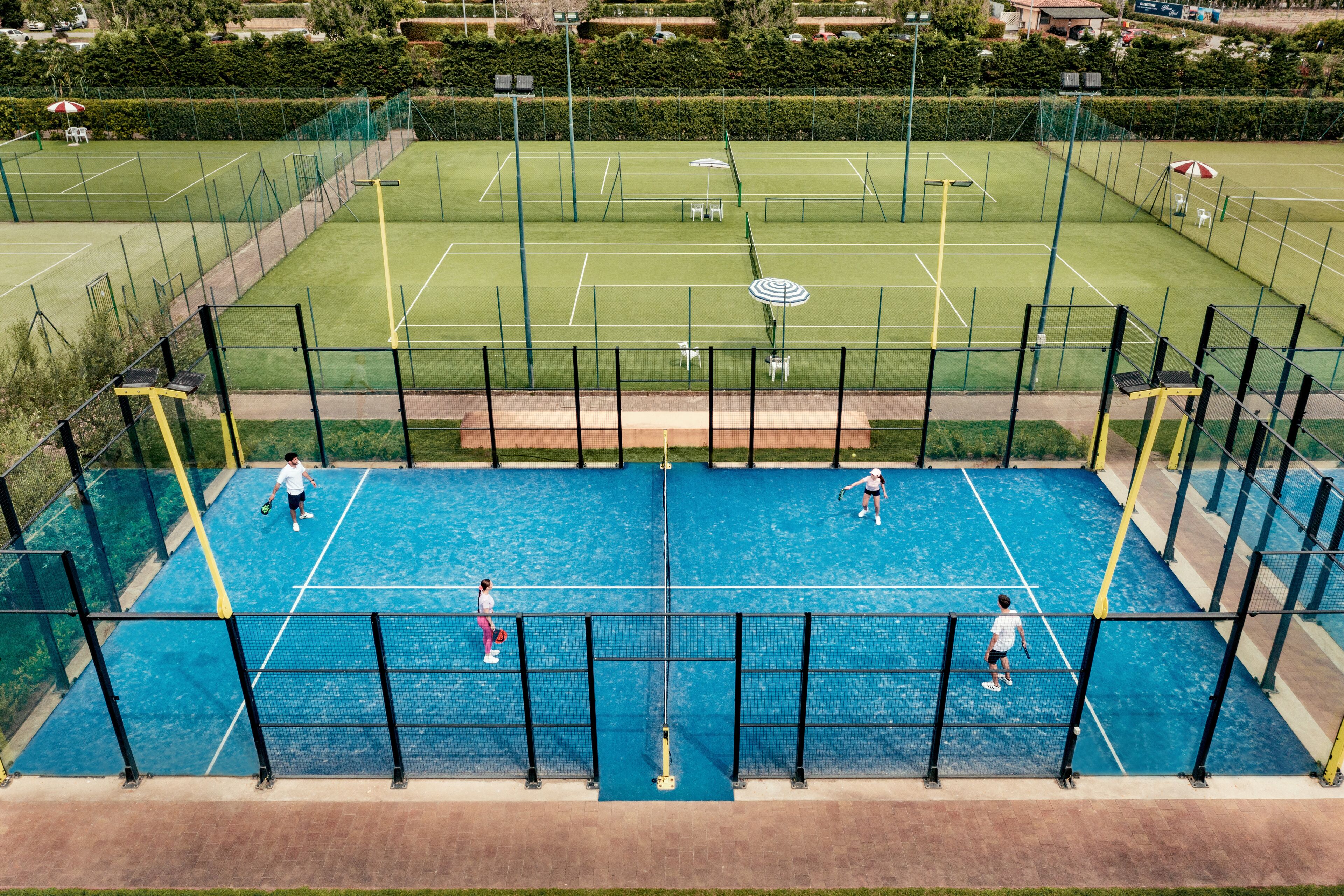 Pista de tenis interior con varias canchas, una red y un área de descanso con sombrillas.
