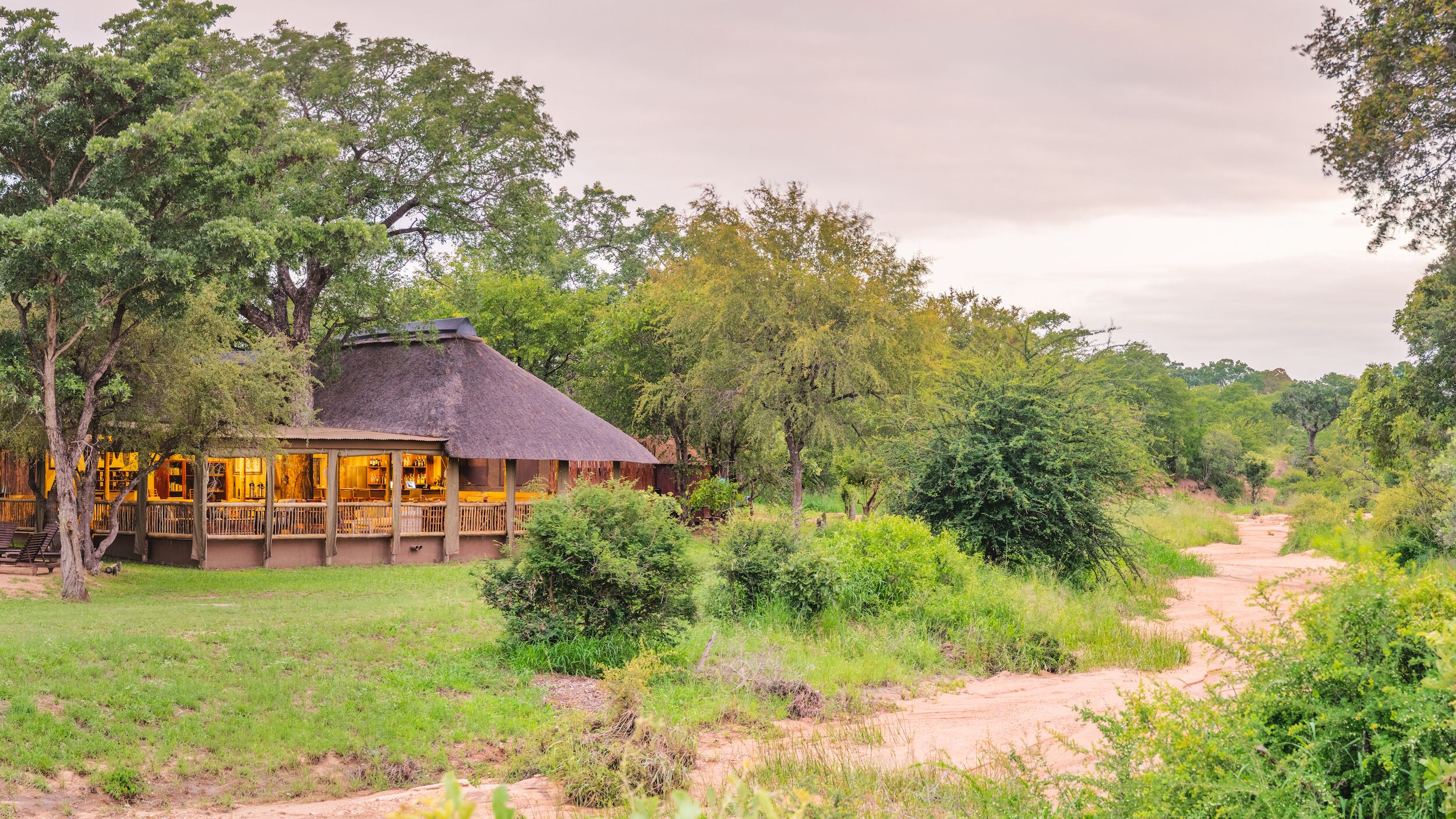 A thatched-roof building with a wooden deck, surrounded by lush greenery and trees.