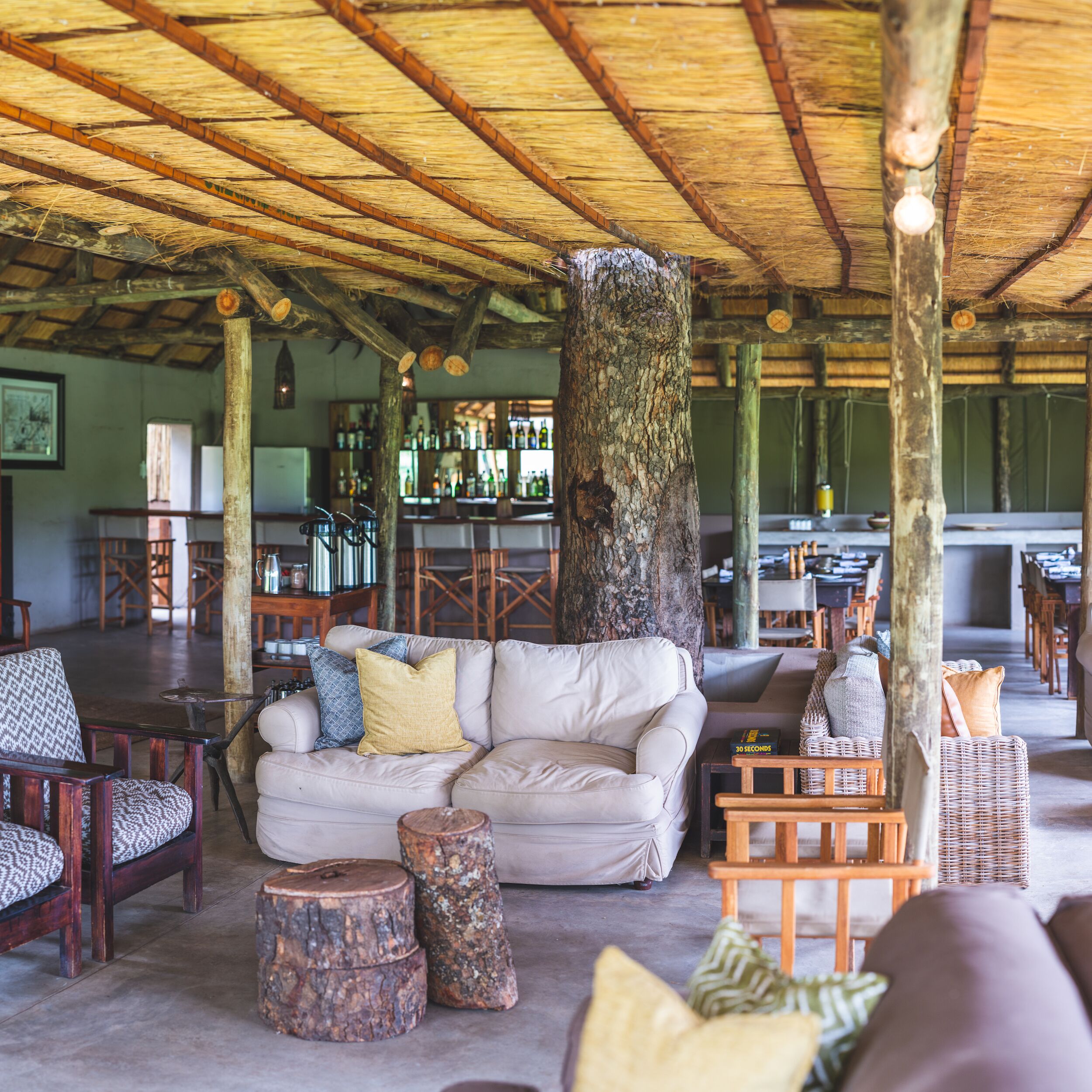 A cozy lounge area with a wooden ceiling, a white sofa with cushions, and rustic wooden stools.