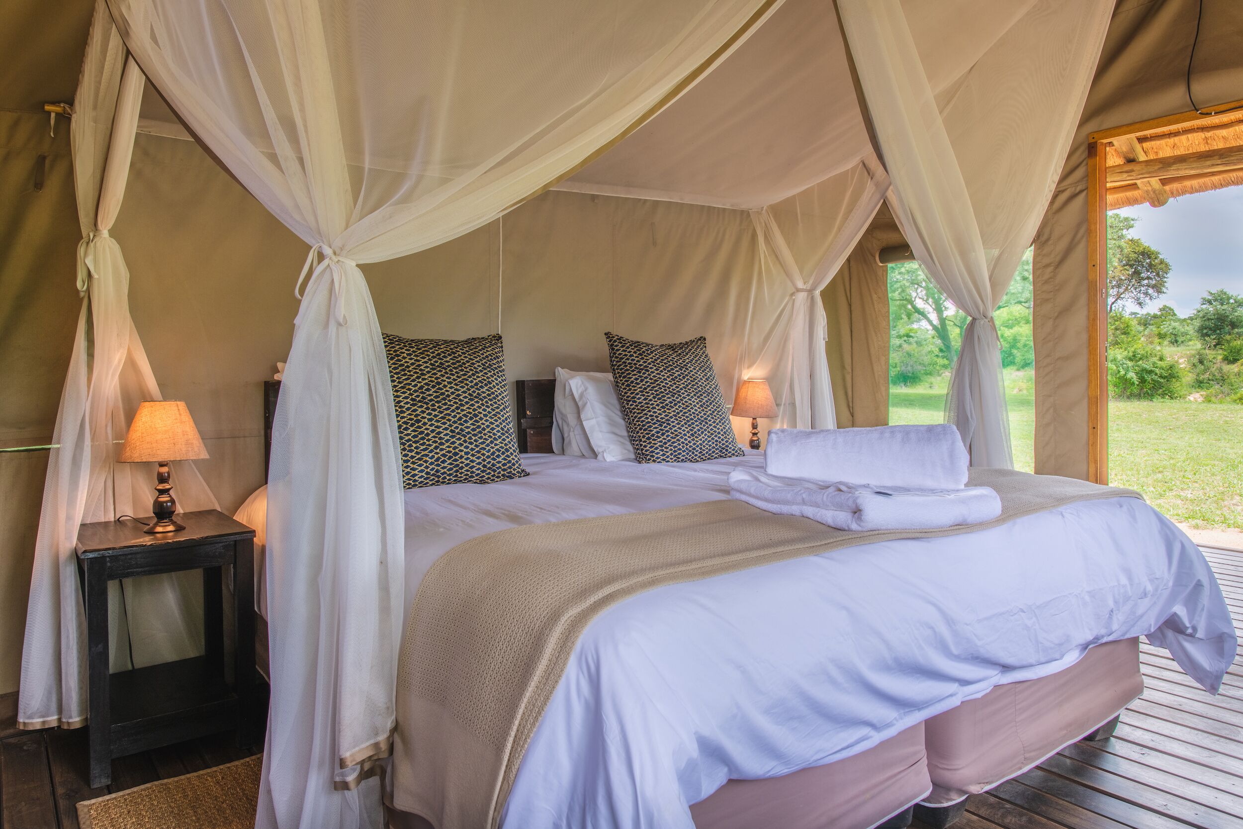 A bed with a canopy, two bedside tables, and a view of the outdoors.