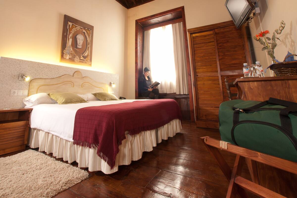 Una habitación de hotel con cama, televisión, techo de madera y ventana.