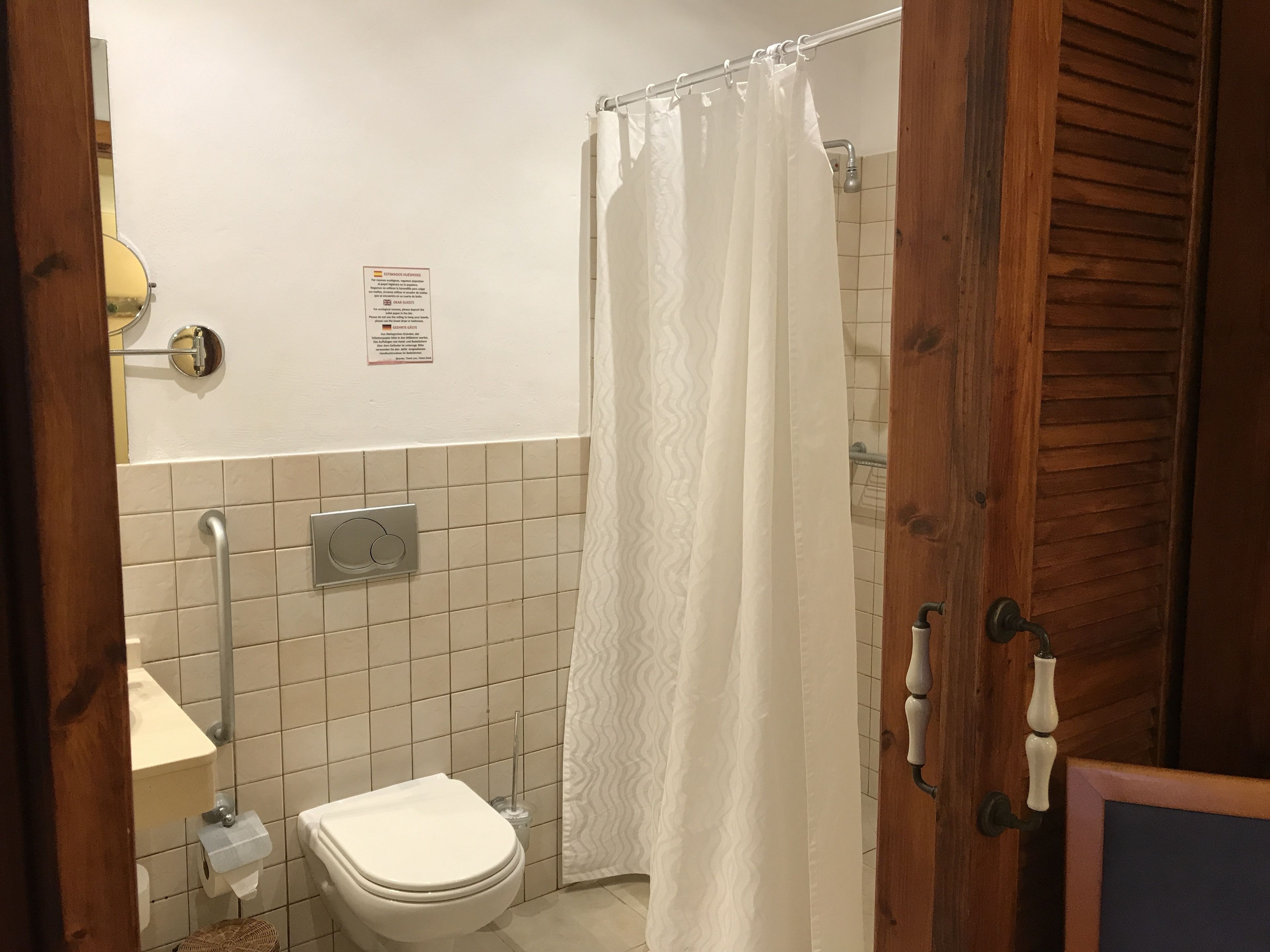 Un baño con inodoro blanco, barra de apoyo, toallero y cortina de ducha.