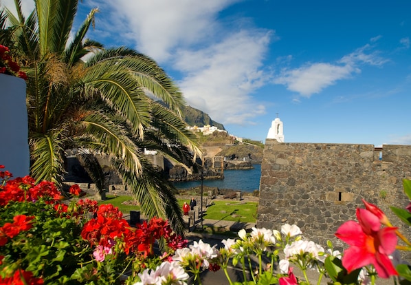 A coastal view with a white church, stone walls, and red flowers in the foreground.