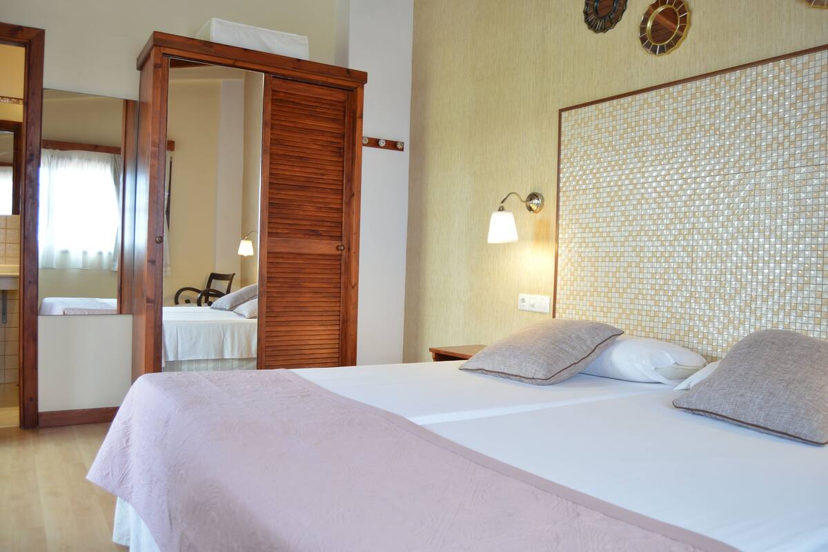Un dormitorio con cama, armario de madera, mesita de noche y lámpara de pared.