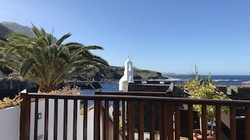 Un balcón con vistas al mar, una iglesia blanca y una palmera.