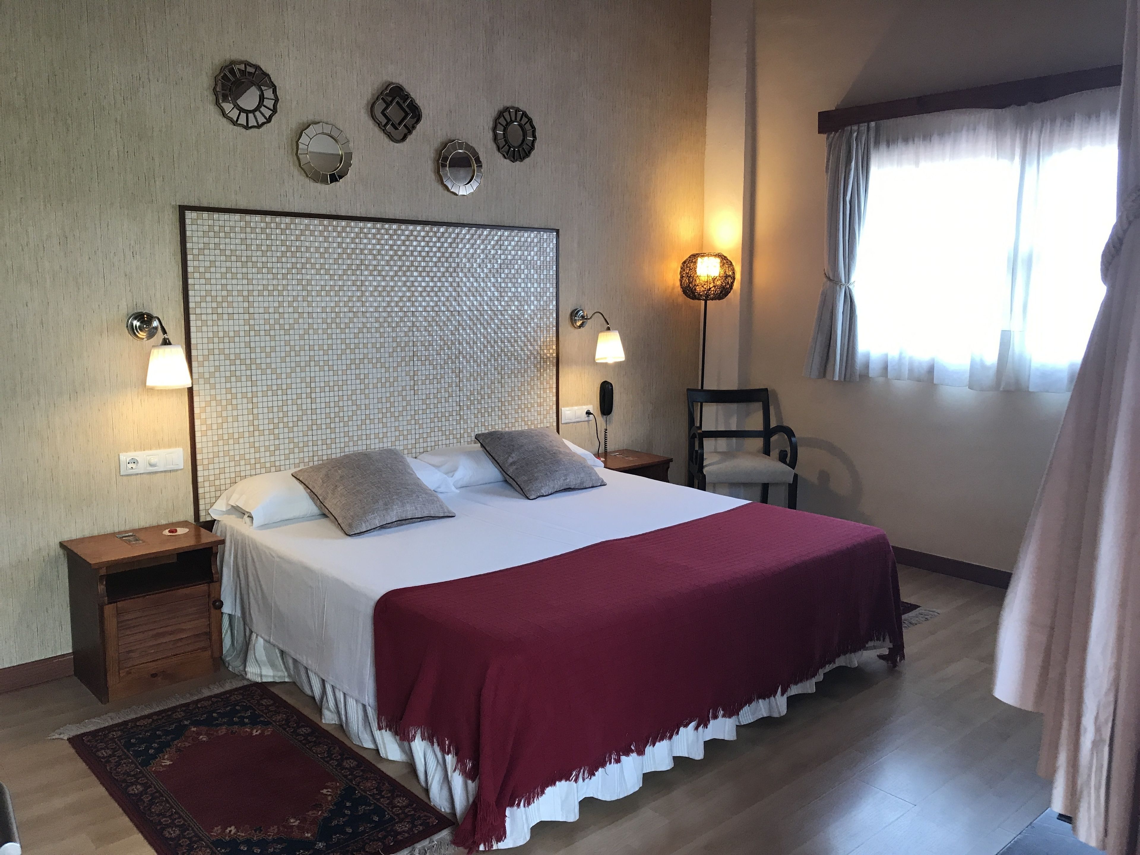 A hotel room with a large bed, two bedside lamps, a wall clock, and a window with curtains.