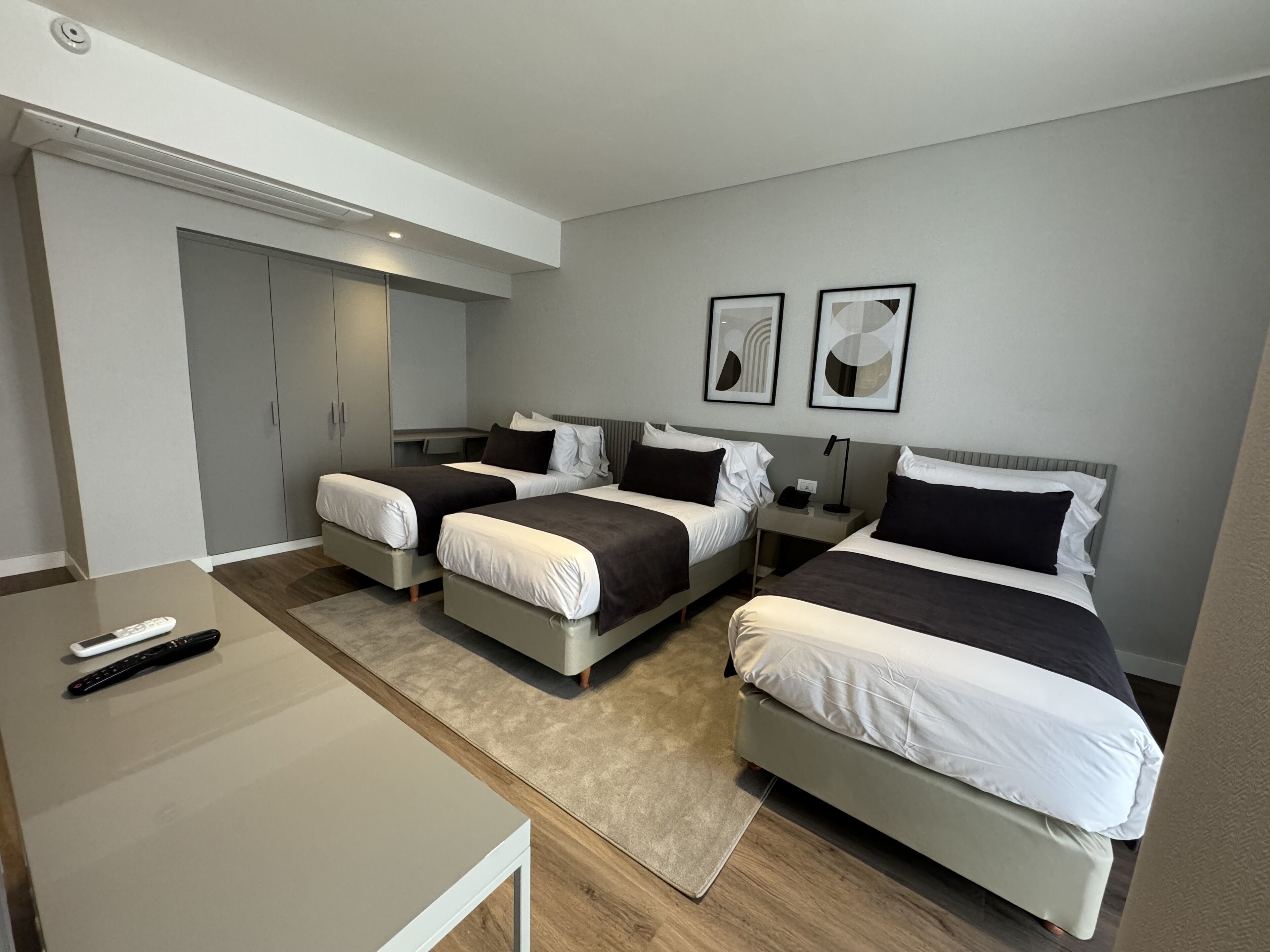 A modern hotel room with two single beds, a small table, and a desk.
