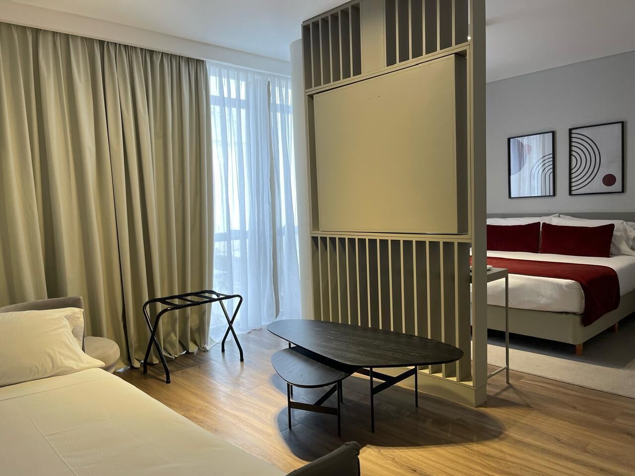 A hotel room with a bed, a table, a chair, a radiator, and artwork on the wall.