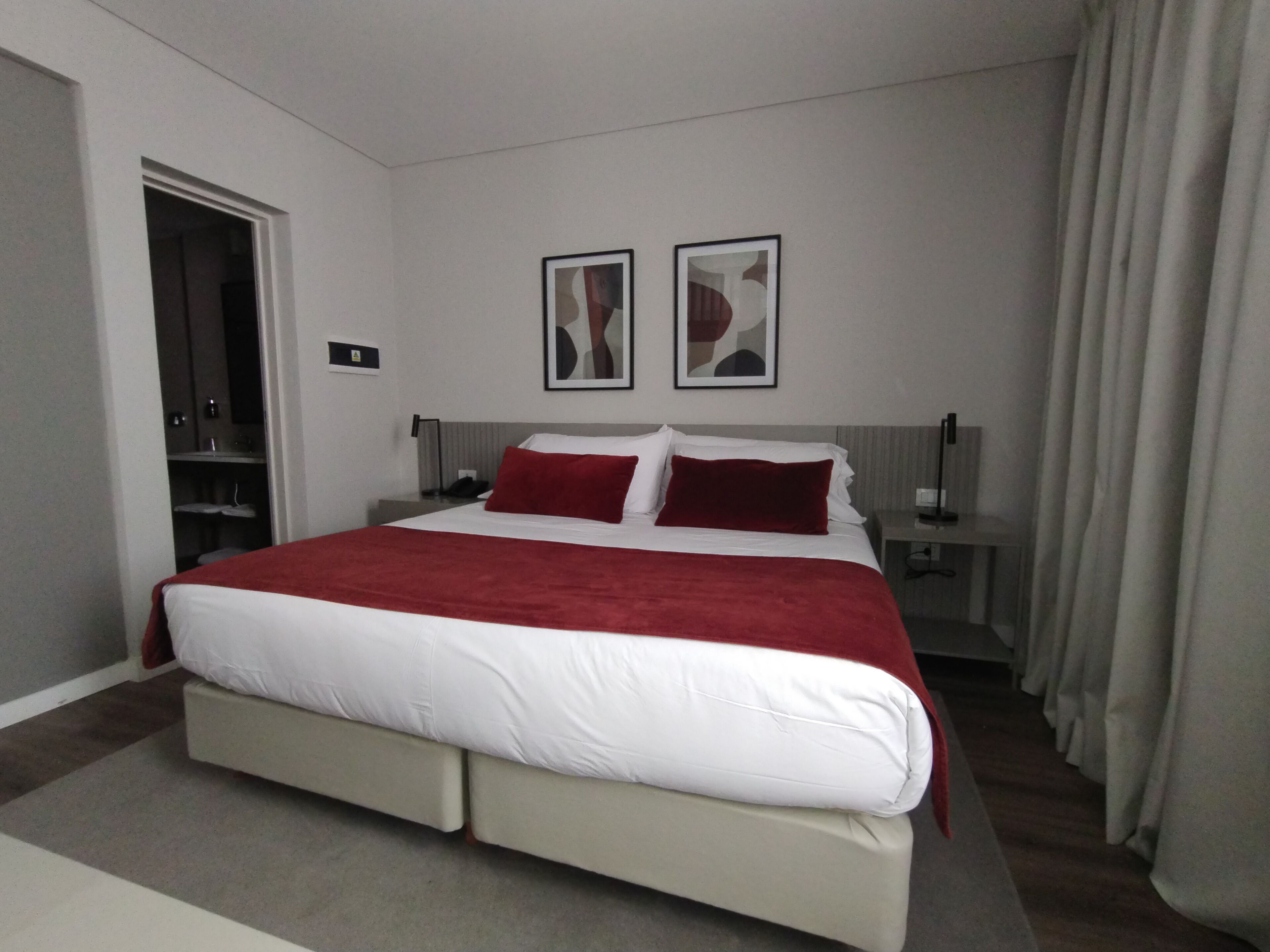 A modern hotel room with a large bed, a nightstand, a desk, and a wardrobe.