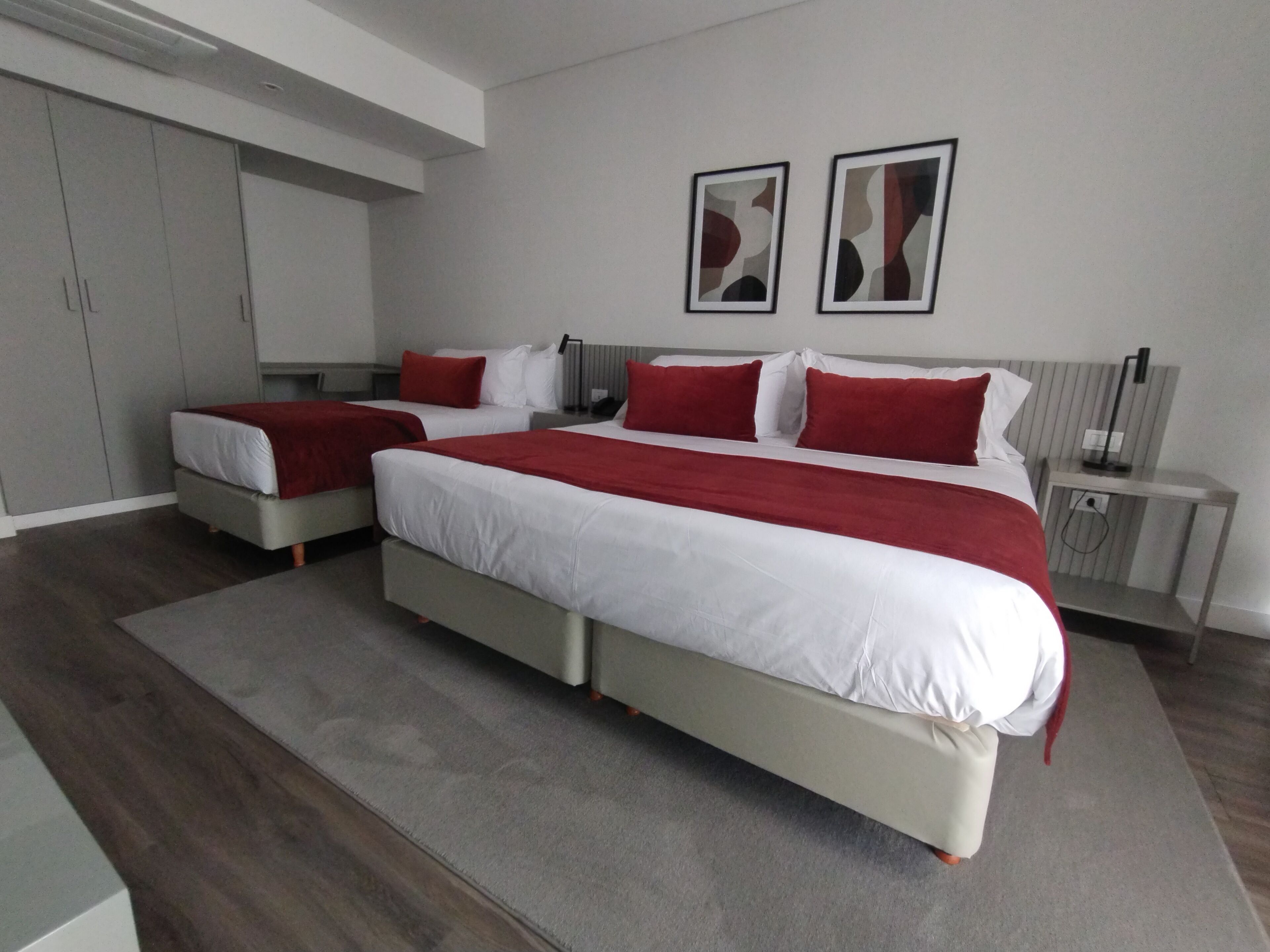 A modern bedroom with two beds, a wardrobe, and artwork on the wall.
