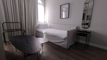 Habitació moderna i minimalista amb un sofà blanc, una taula rodona petita, una cadira de metall negre i un mirall sobre una taula auxiliar.