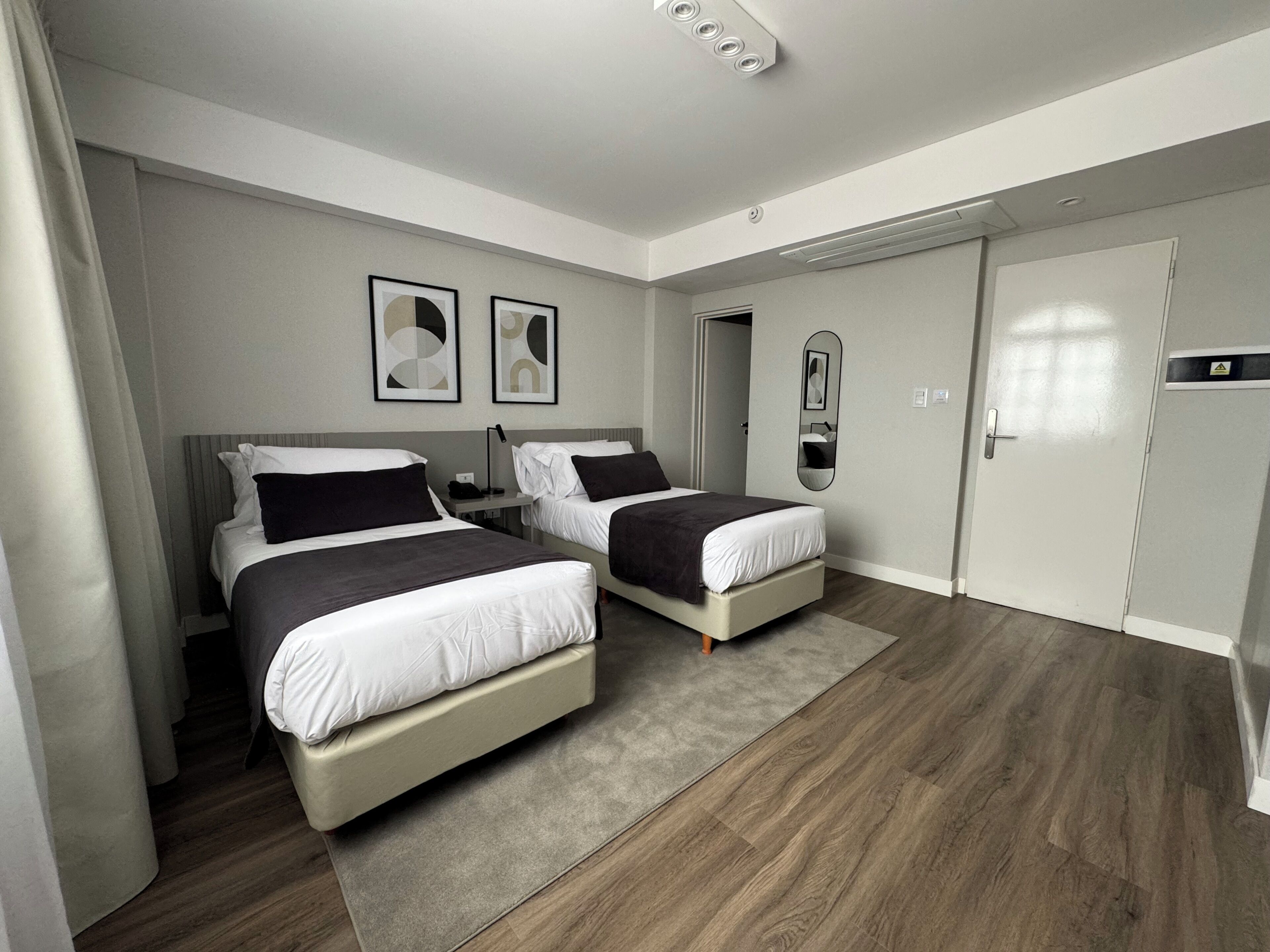Una habitación de hotel moderna con dos camas, un espejo grande y un armario.