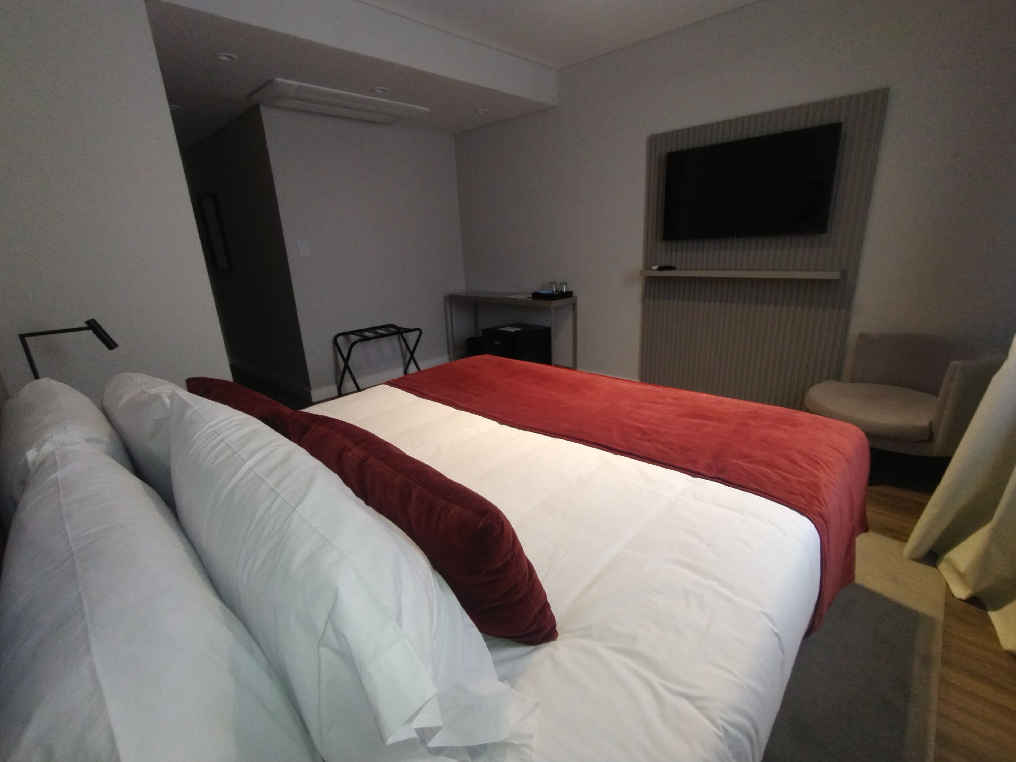 A hotel room with a bed, a TV mounted on the wall, a chair, and a desk.
