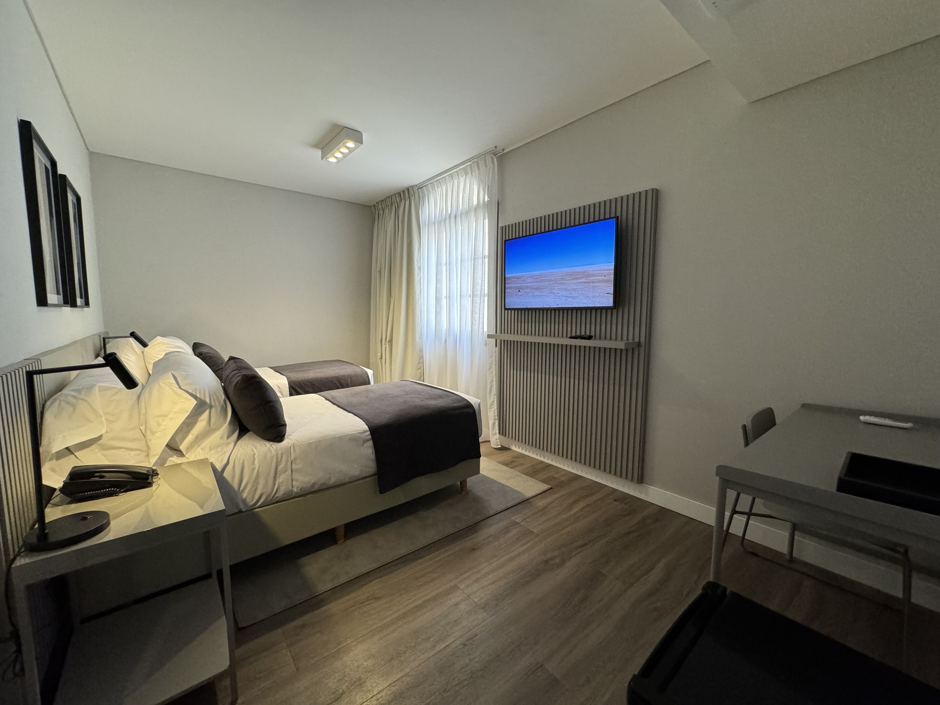 A modern bedroom with a bed, bedside table, TV, and a desk with a chair.
