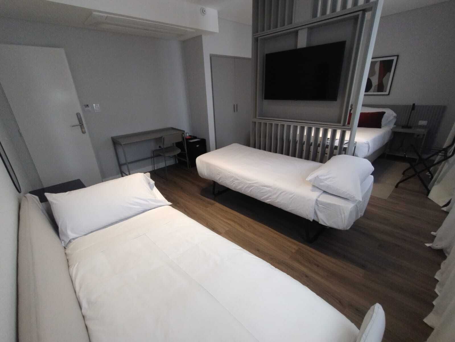 Ein Hotelzimmer mit zwei Einzelbetten, einem Schreibtisch, einem Stuhl, einem Fernseher und einer Heizung.