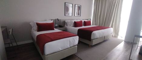 Una habitación de hotel moderna con dos camas, un ventanal con cortinas, una silla y un escritorio.