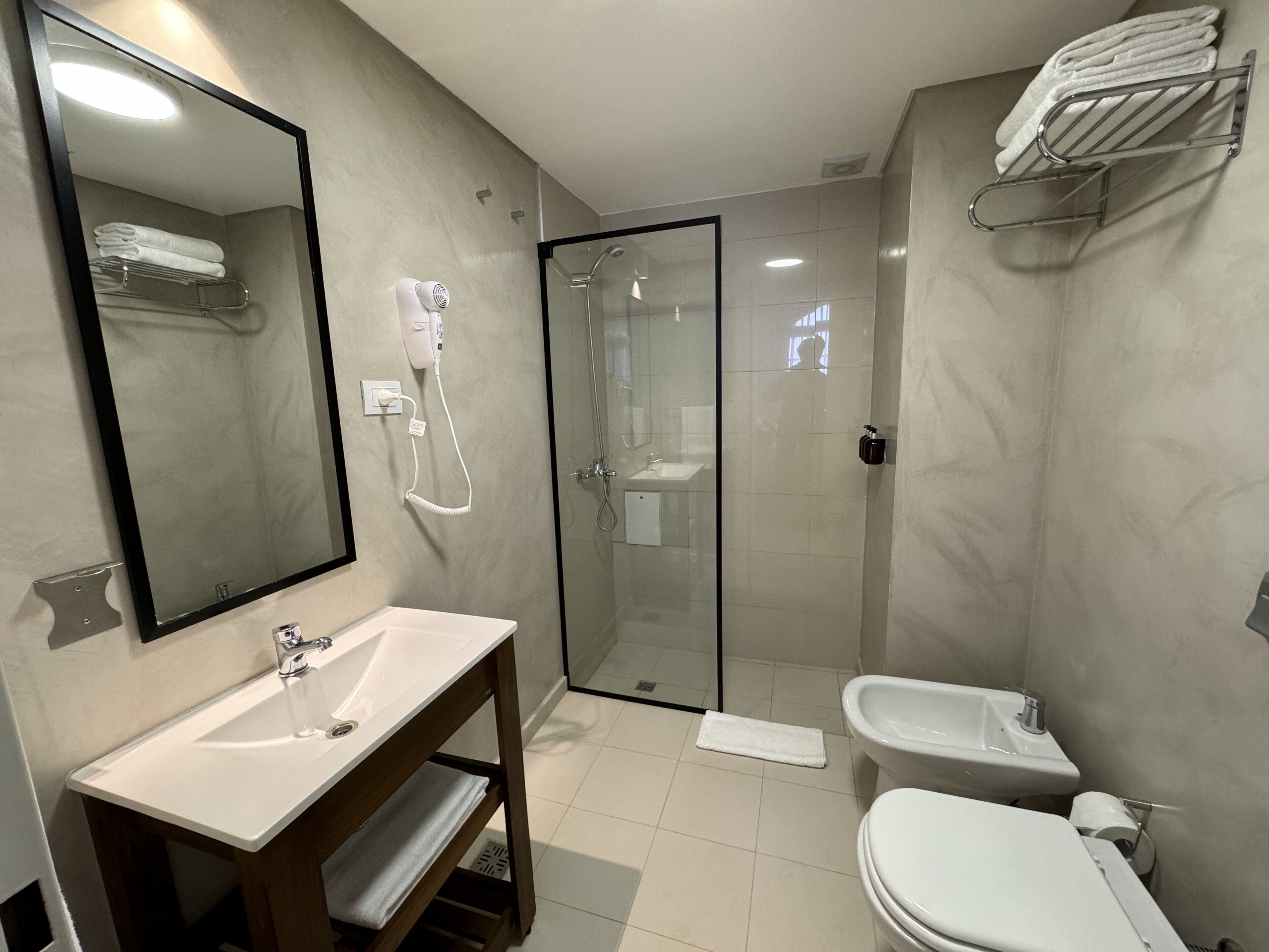 A modern bathroom with a sink, mirror, towel rack, shower, and toilet.