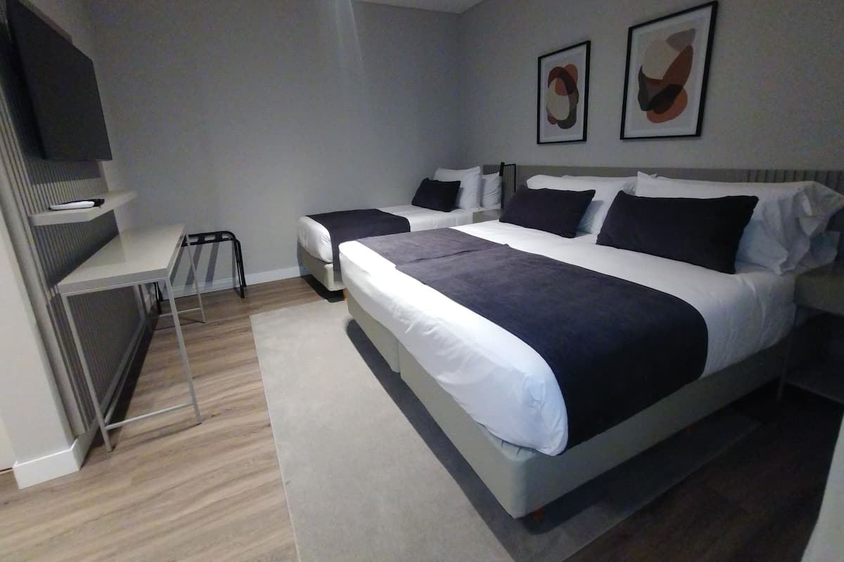 Ett modernt hotellrum med en stor säng, ett skrivbord och en stol. På väggen hänger två inramade tavlor.