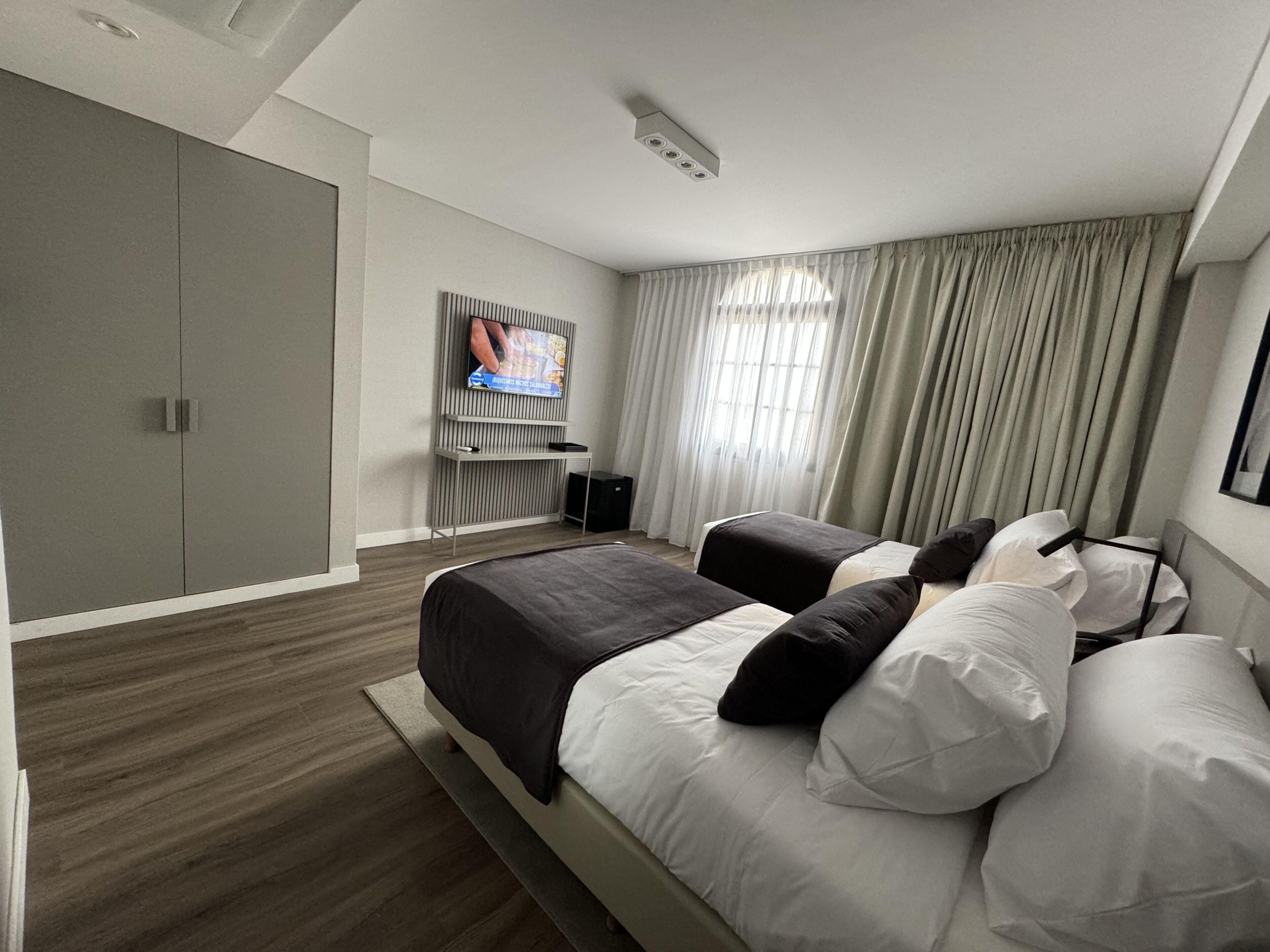 A modern hotel room with a large bed, a TV mounted on the wall, and a wardrobe.