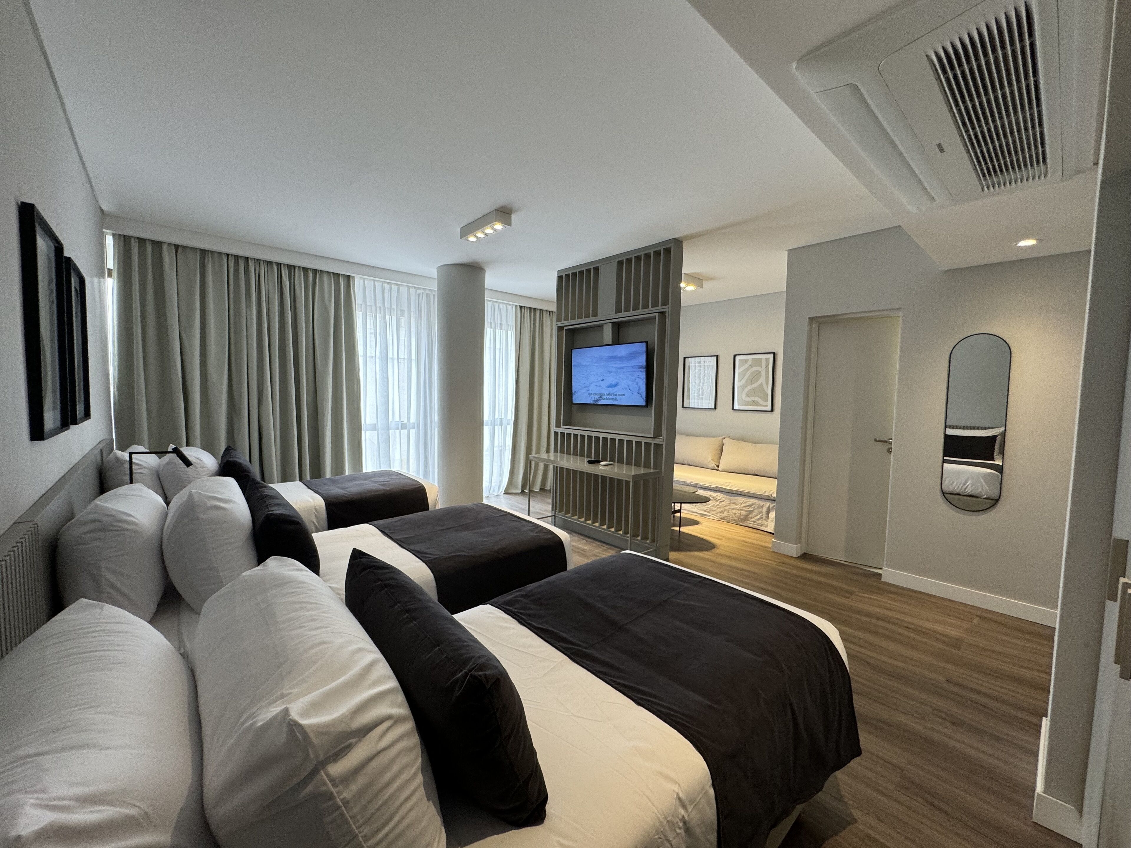 A modern hotel room with a large bed, a TV, a sofa, and a mirror.