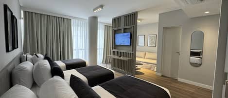 Una habitación de hotel moderna con una cama grande, televisión, sofá y espejo.