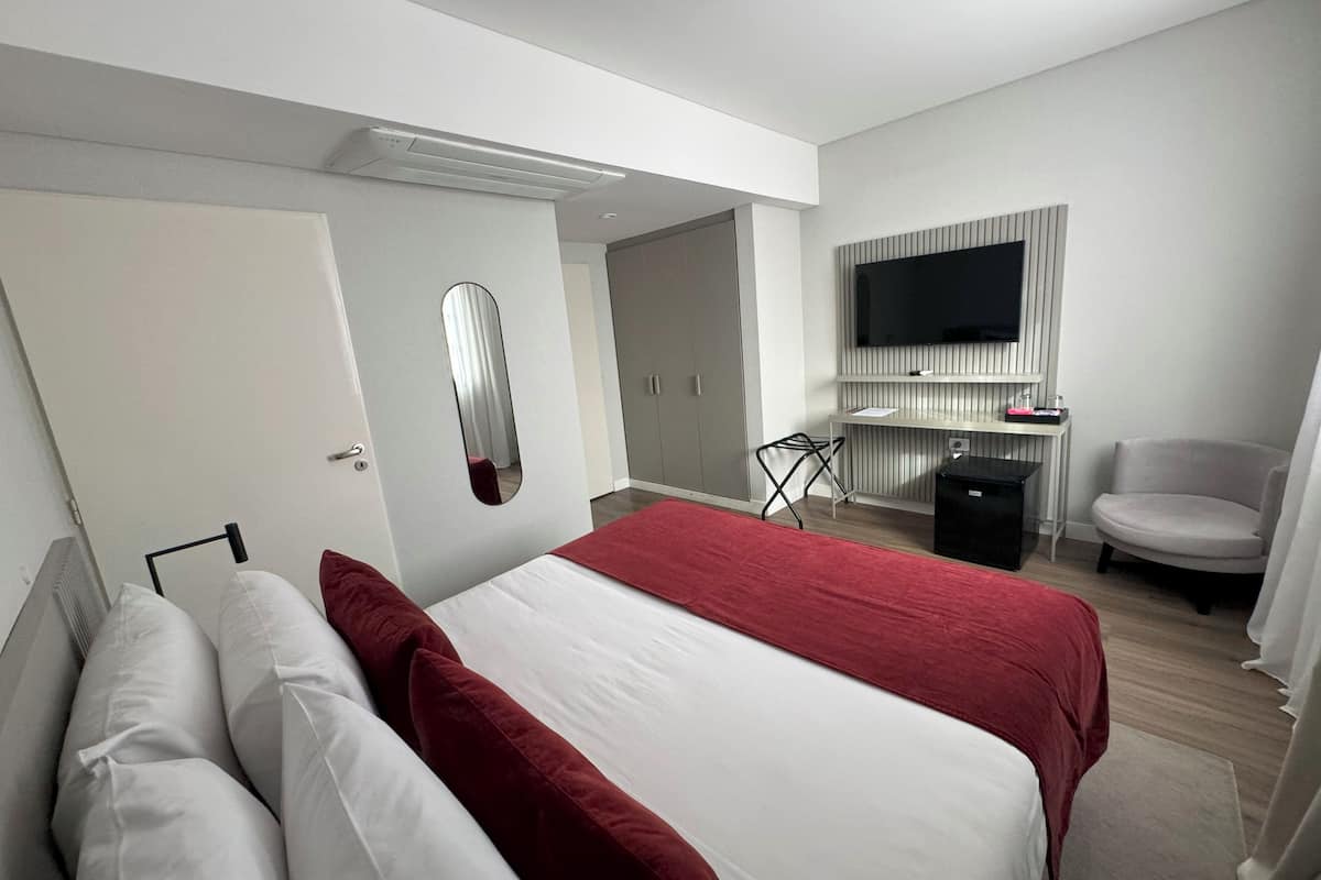 Ett modernt hotellrum med en stor säng, en tv som är monterad på väggen och ett skrivbord med en stol.