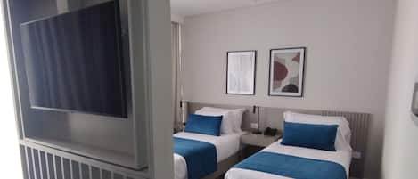 A hotel room with two beds, a TV, and artwork on the wall.