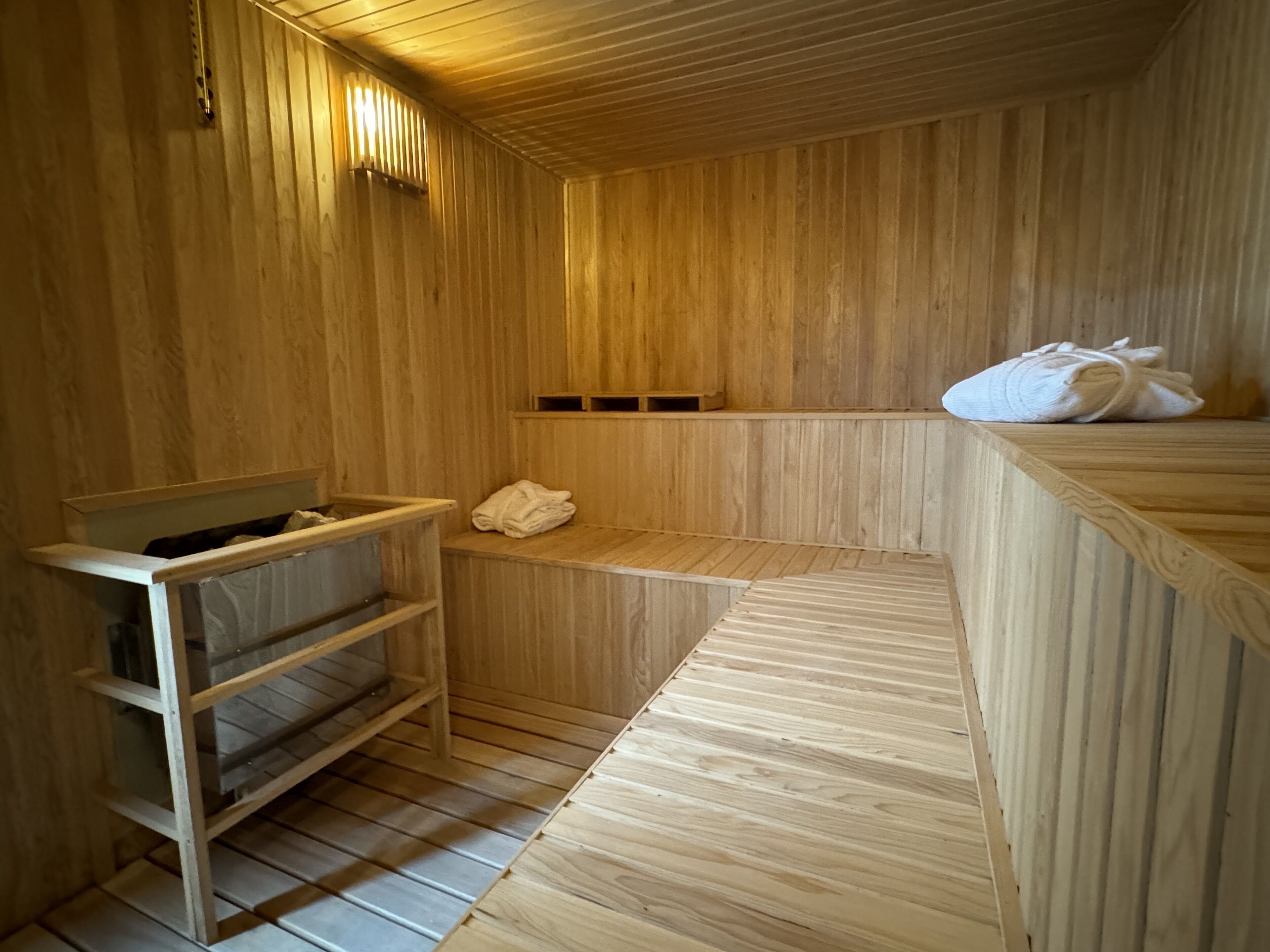 A wooden sauna room with benches, a shelf, and towels.
