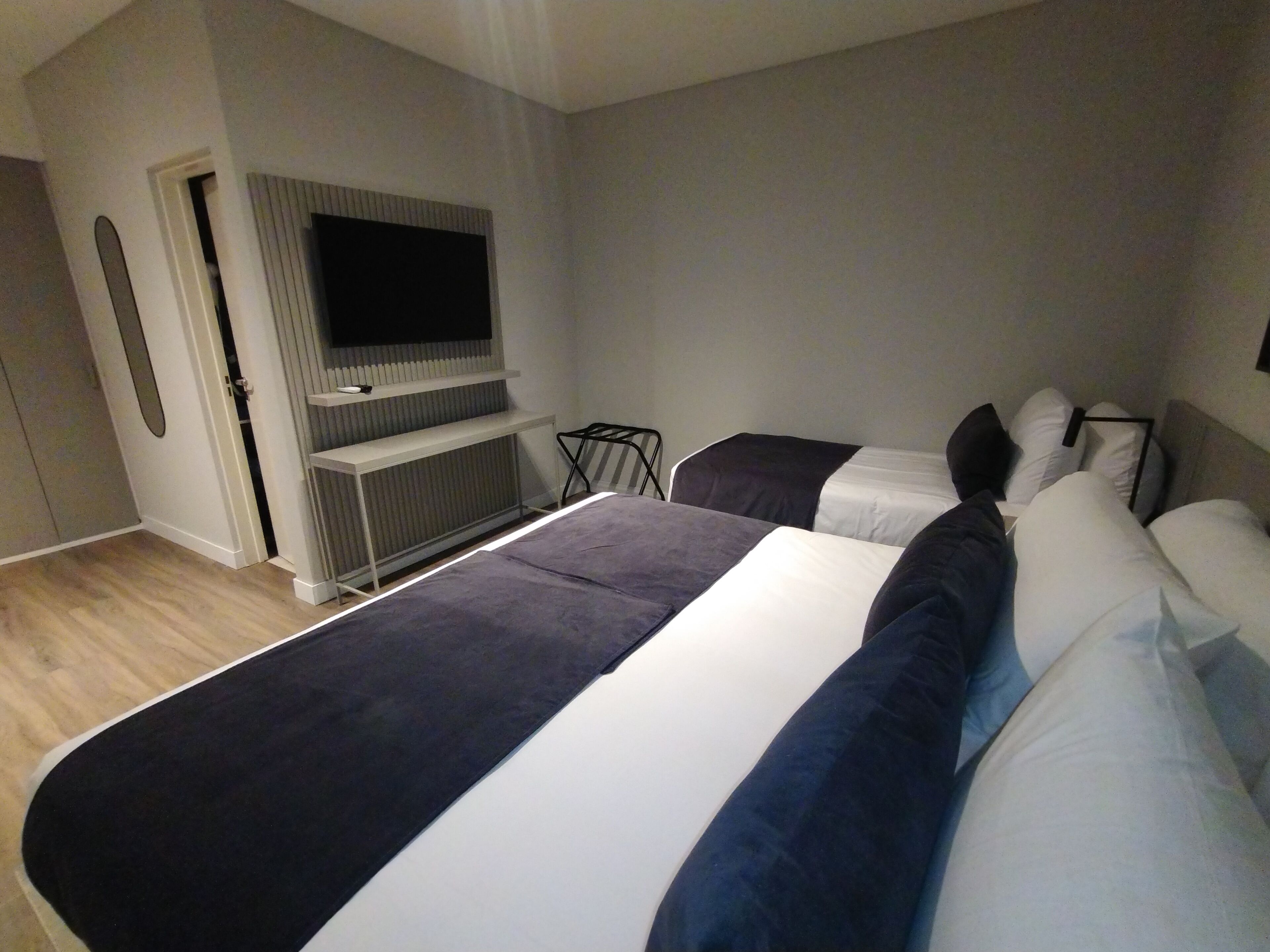 A modern hotel room with a large bed, a TV mounted on a wall, and a small seating area.