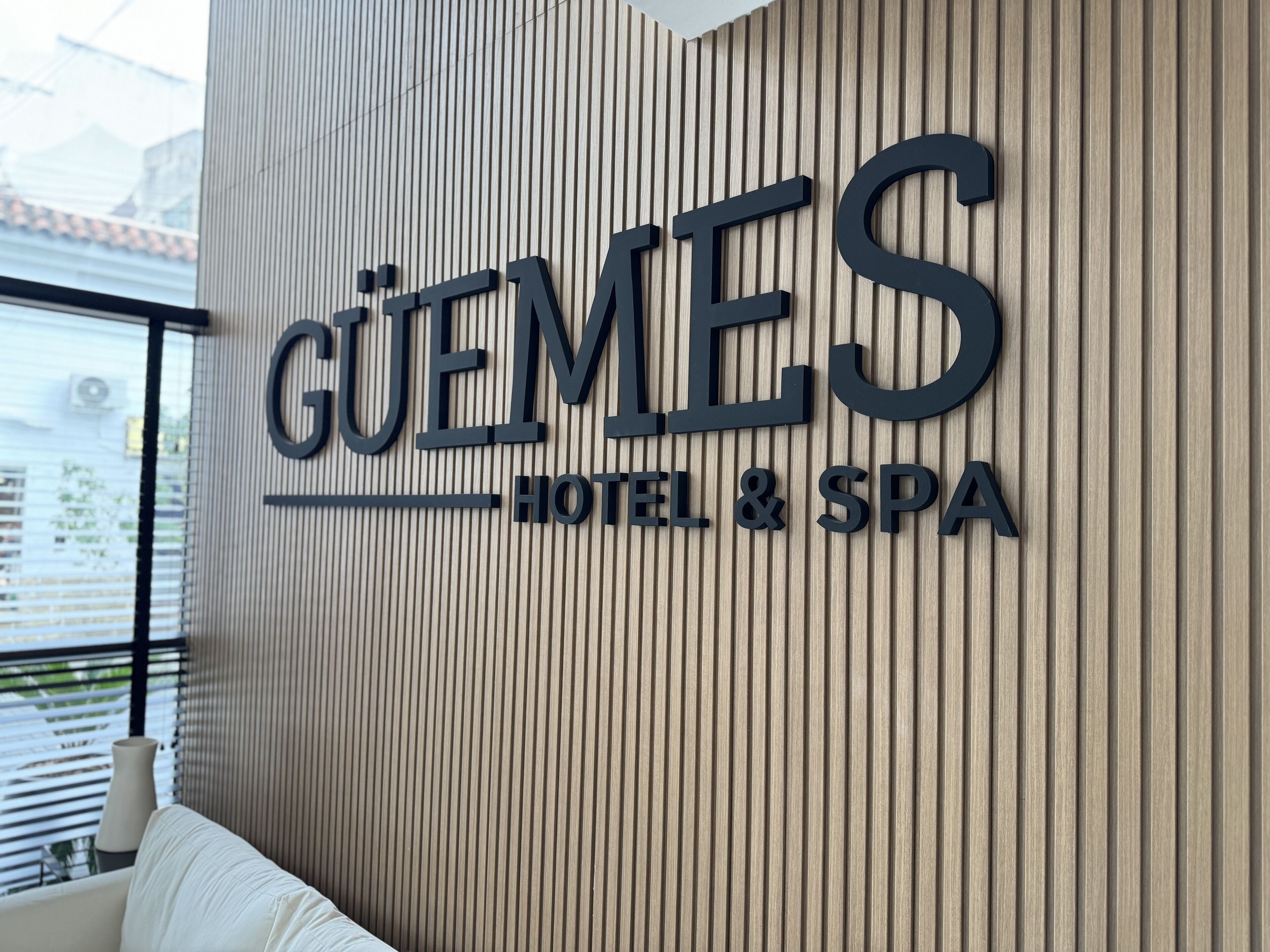 A hotel sign with the name "GUEMES HOTEL & SPA" on a wooden panel wall.