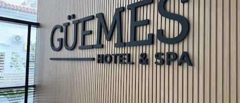 A hotel sign with the name "GUEMES HOTEL & SPA" on a wooden panel wall.