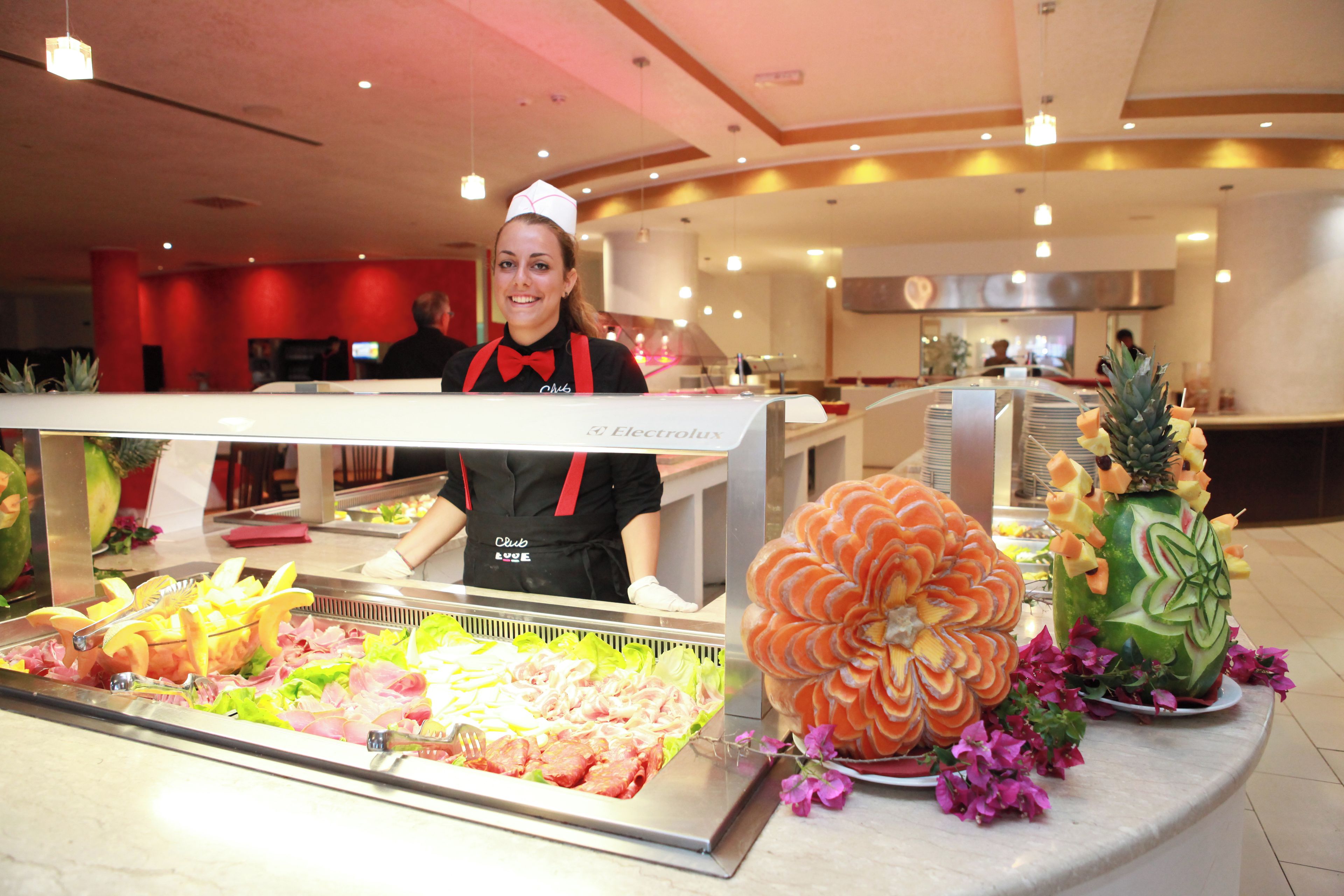 Ein Buffet mit einer Auswahl an Speisen, darunter Obst und Gemüse, sowie eine Person, die den Tresen bedient.