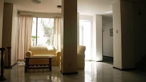 A living room with a sofa, a coffee table, and a chair. There is a large window with curtains, and a door leading to another room. - RJ Hotel del Sol (Mendoza)