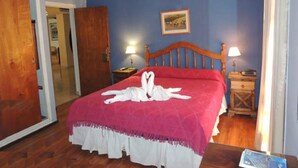 A bedroom with a wooden bed, a red bedspread, two bedside lamps, and a framed picture on the wall. - RJ Hotel del Sol (Mendoza)