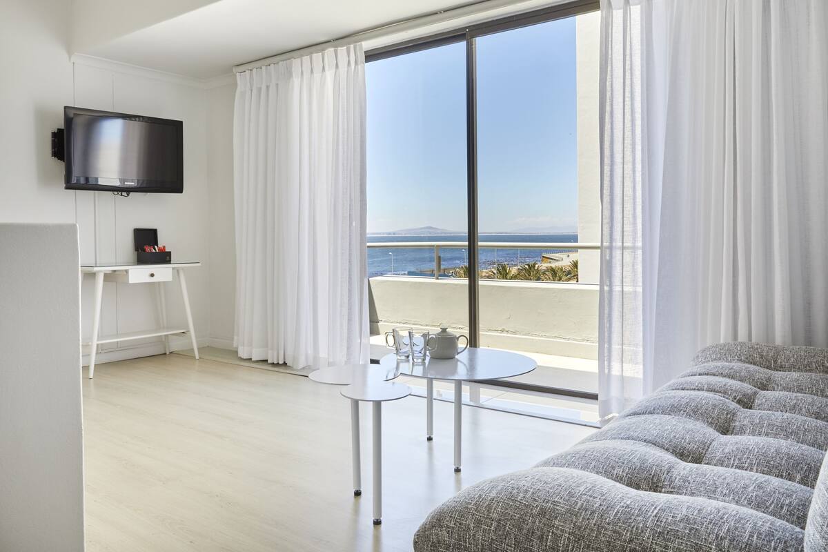 Ett modernt hotellrum med en stor balkong, en platt-TV, ett litet bord med en tekanna och en bekväm soffa.
