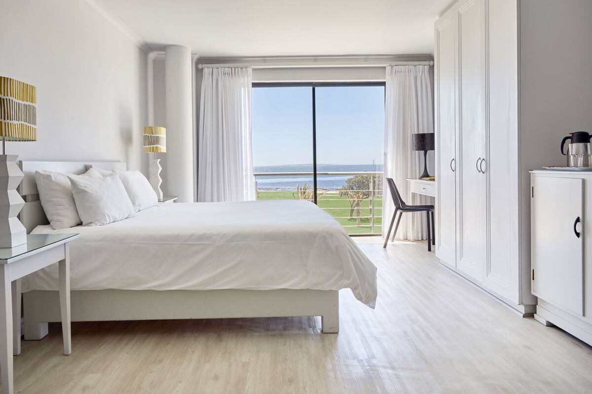 Ett hotellrum med en stor säng, ett skrivbord, en stol och utsikt över havet.