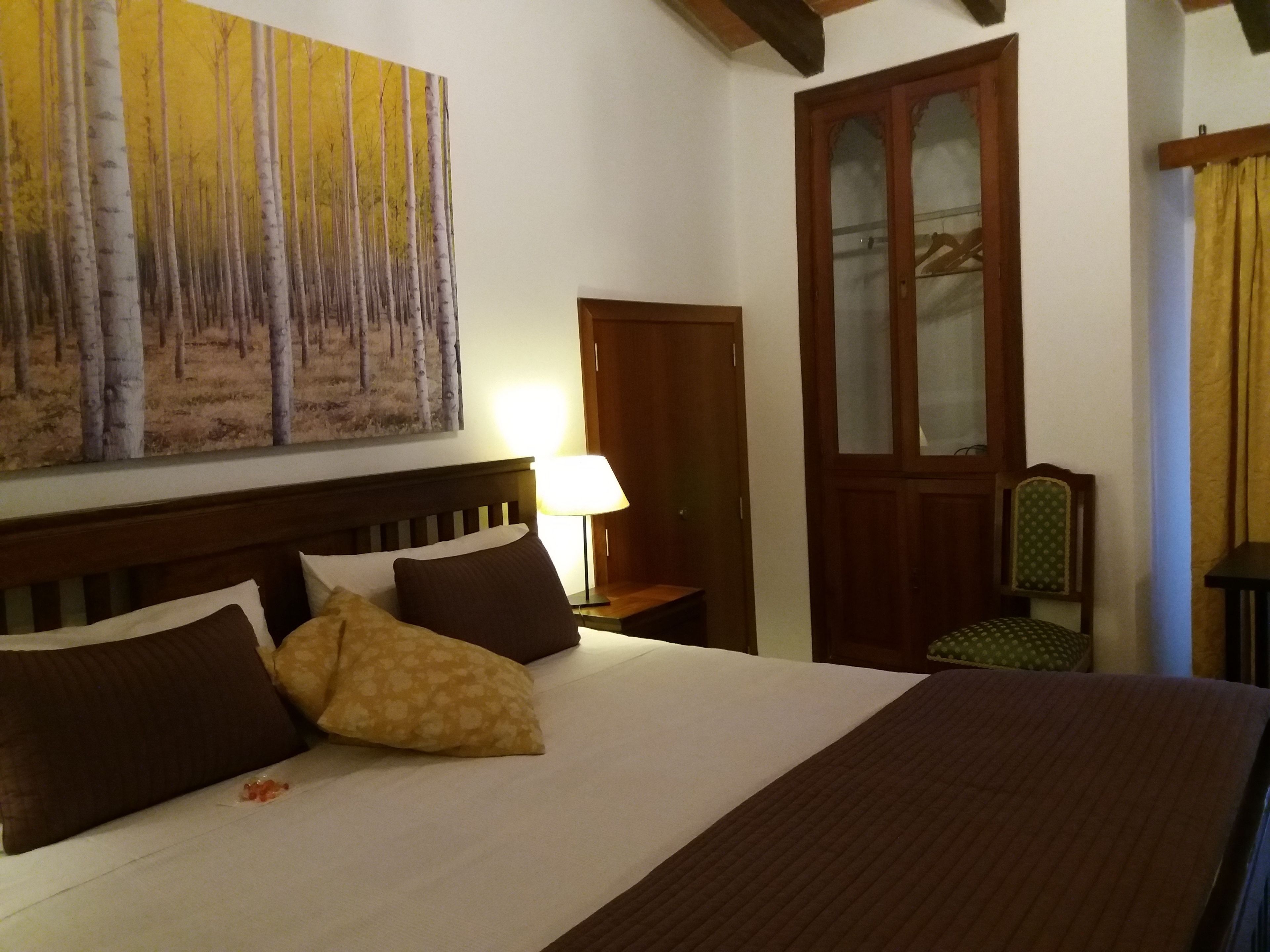 Quarto com uma cama grande, cabeceira de madeira, pintura de árvores, guarda-roupa de madeira e uma cadeira.