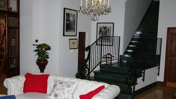 Una sala de estar con un sofá blanco, una araña, una escalera y cuadros en la pared.
