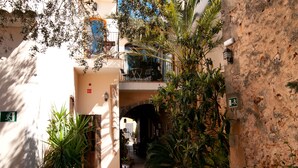 A narrow alleyway with a stone wall, a wooden door, and a small balcony with a table and chairs.