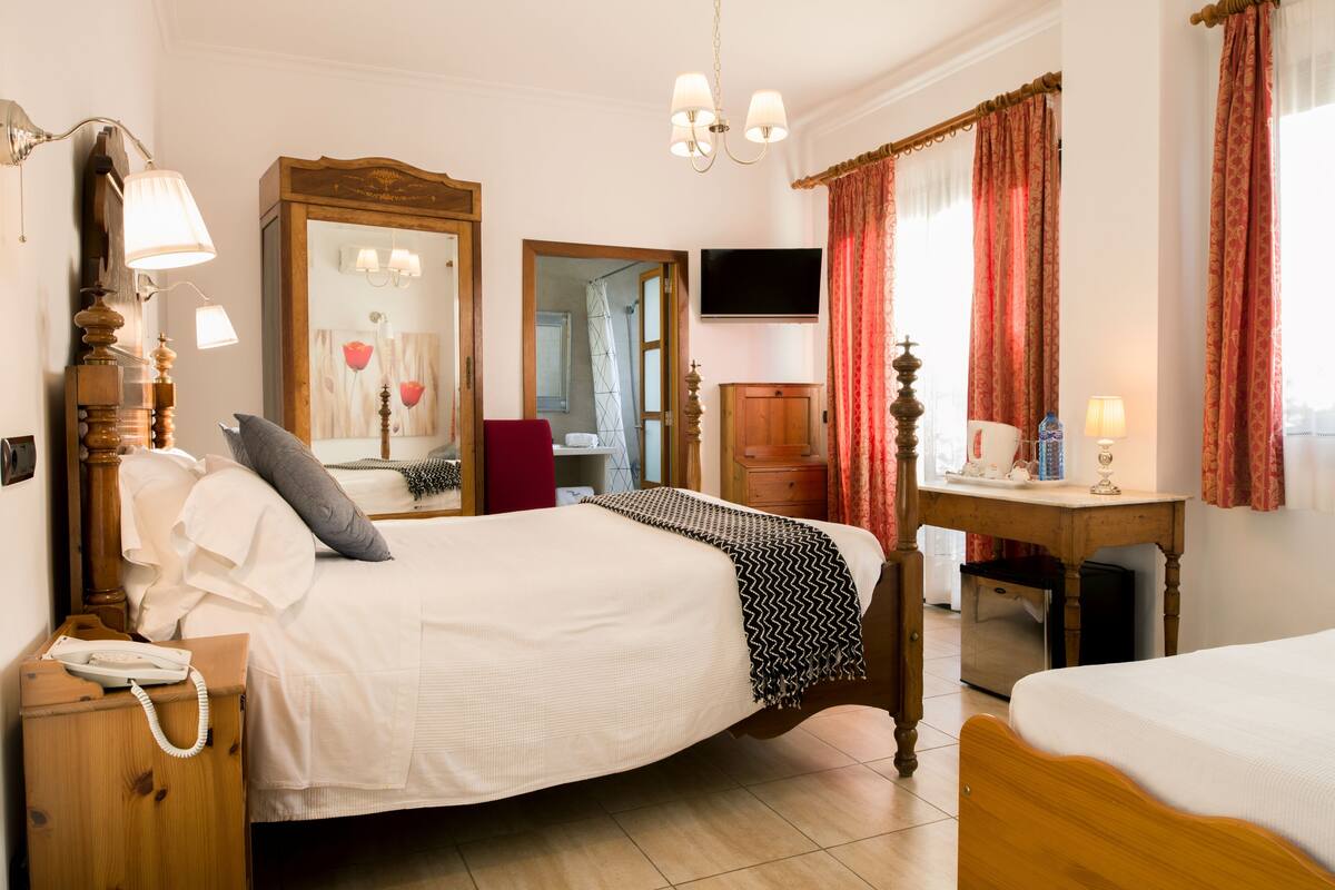 Habitación de hotel con una cama grande, mesita de noche, lámpara, espejo, televisor y escritorio con una silla.