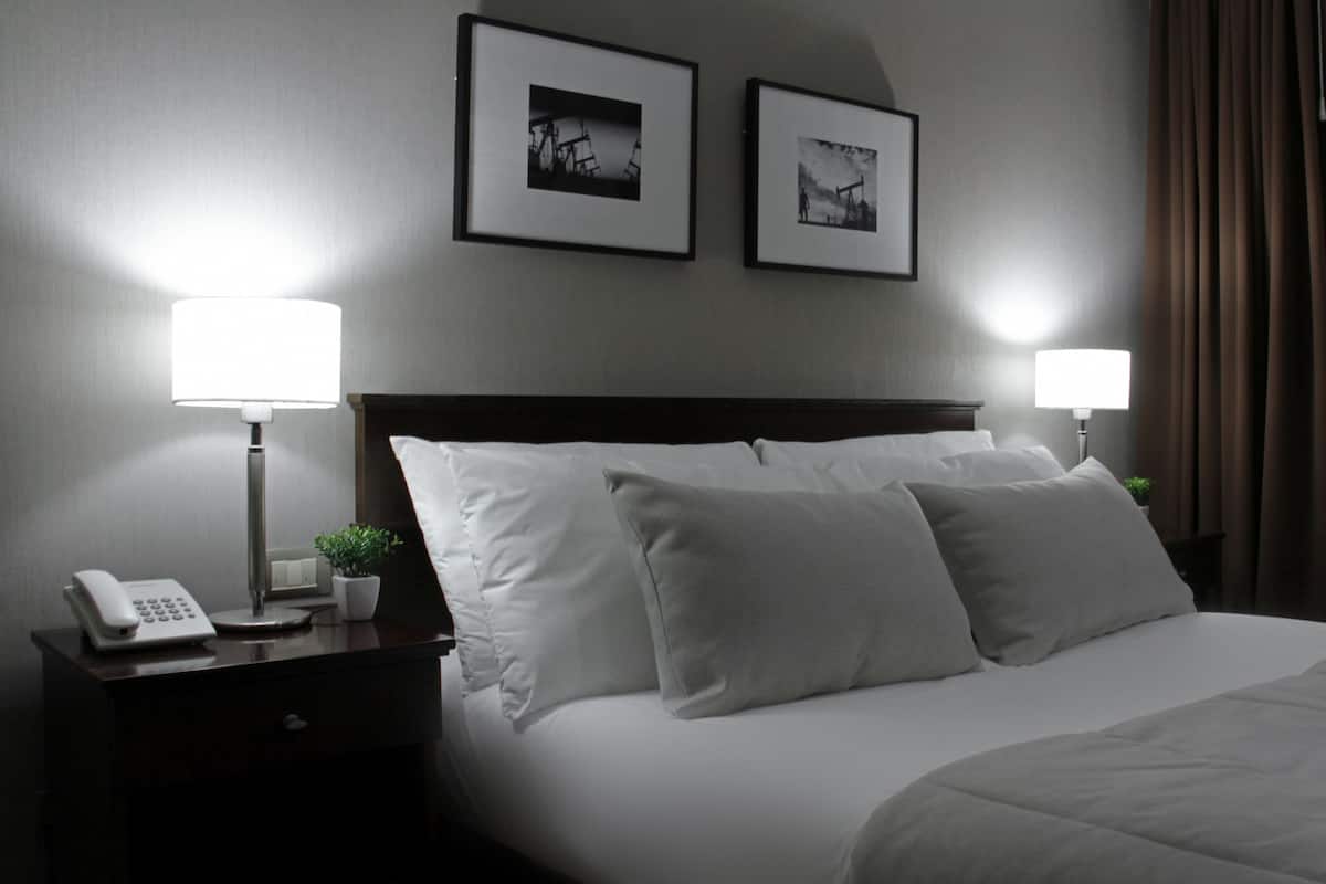 A hotel room with a neatly made bed, two bedside lamps, a phone on a bedside table, and two framed pictures on the wall.