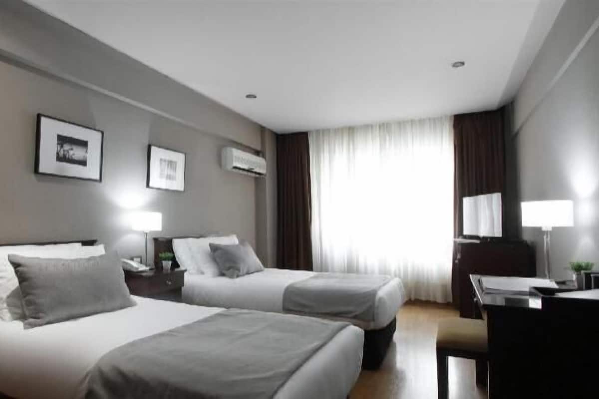 A hotel room with two beds, a desk, a chair, a lamp, and a window with curtains.